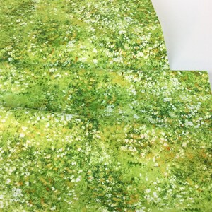 May include: Green fabric with a meadow-like pattern. The fabric features a vibrant green base with scattered white and yellow floral accents, creating a natural, grassy appearance. The fabric is folded, showing its texture and design.