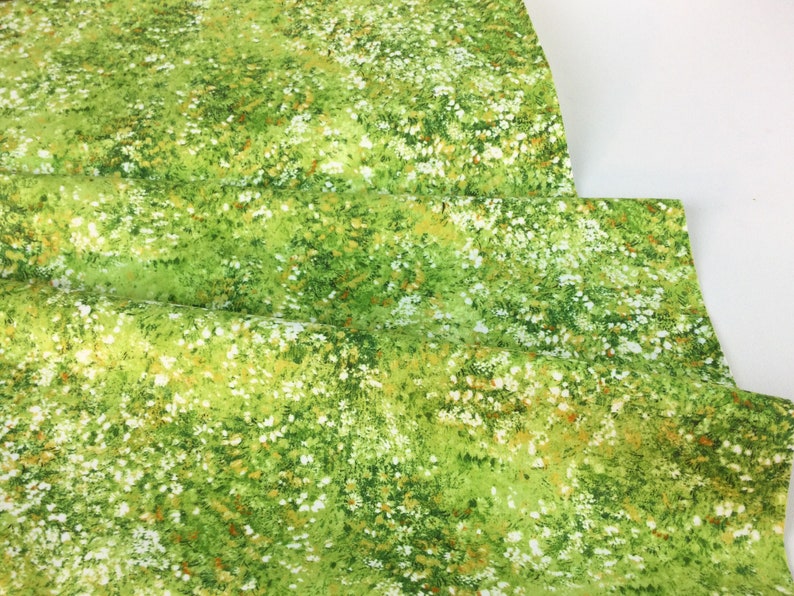 May include: Green fabric with a meadow-like pattern. The fabric features a vibrant green base with scattered white and yellow floral accents, creating a natural, grassy appearance. The fabric is folded, showing its texture and design.
