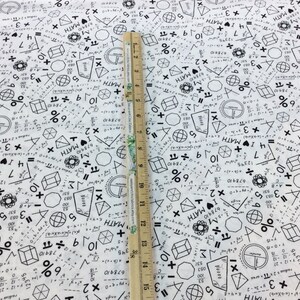 May include: White fabric printed with black mathematical symbols, equations, and the text "I MATH". A wooden ruler, marked in inches, is placed on the fabric, showing measurements up to 15 inches.