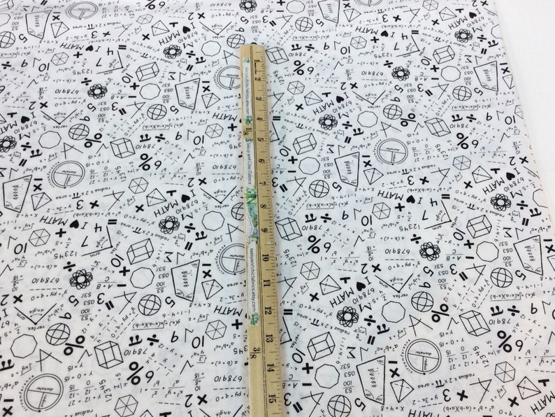 May include: White fabric printed with black mathematical symbols, equations, and the text "I MATH". A wooden ruler, marked in inches, is placed on the fabric, showing measurements up to 15 inches.