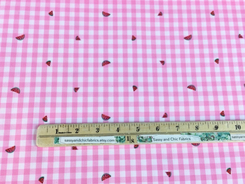 May include: Pink and white gingham fabric with scattered watermelon slice designs. The fabric has a ruler with the text "Sassy and Chic Fabrics etsy.com" on it. The fabric is suitable for sewing projects.