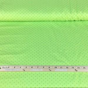 May include: Bright green fabric with small, evenly spaced, darker green polka dots. A wooden ruler with inch measurements is placed on the fabric. The fabric is rolled up in the background. The website address "sassyandchicfabrics.etsy.com" is printed on the ruler.