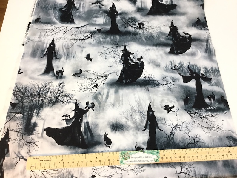 May include: Fabric with a black and white Halloween design. Silhouetted witches in tall hats and flowing gowns are scattered across a misty forest scene. Black cats and crows are also featured. The fabric is printed on a white background.