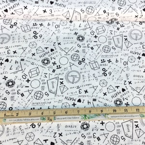 May include: White fabric printed with black math symbols, equations, and the phrase "I ❤️ MATH." Geometric shapes, numbers, and formulas are scattered across the material. A wooden ruler with inch markings is at the bottom.