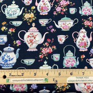 May include: Fabric with a repeating pattern of teapots, teacups, and floral arrangements in pink, blue, and white on a navy blue background. A ruler shows measurements in inches. The text "sassyandchicfabrics.etsy.com" is visible.