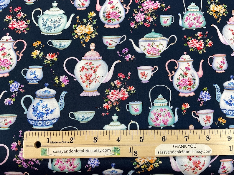 May include: Fabric with a repeating pattern of teapots, teacups, and floral arrangements in pink, blue, and white on a navy blue background. A ruler shows measurements in inches. The text "sassyandchicfabrics.etsy.com" is visible.