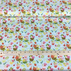 May include: Light blue fabric with a repeating pattern of tropical drinks, fruit baskets, and fruit slices. The design includes pineapples, watermelons, strawberries, and kiwi. The fabric is printed with a ruler for measurement.