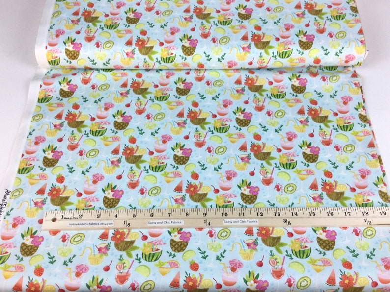 May include: Light blue fabric with a repeating pattern of tropical drinks, fruit baskets, and fruit slices. The design includes pineapples, watermelons, strawberries, and kiwi. The fabric is printed with a ruler for measurement.