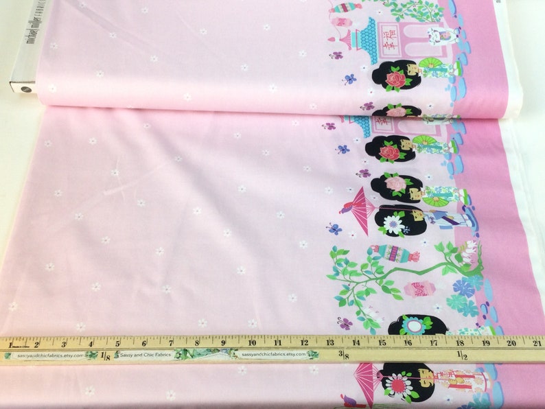 May include: Pink fabric with a repeating border design featuring Asian-inspired illustrations of figures, pagodas, and floral elements. The fabric has a light pink background with small white floral accents.