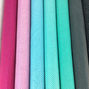 May include: A collection of fabric rolls in various colors, including white, fuchsia, light pink, turquoise, teal, gray, and black. Each fabric features a repeating pattern of small, square-shaped dots. The rolls are tightly wound, showcasing the fabric's texture and color variations.