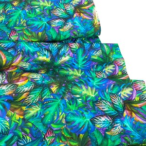 May include: Fabric with a vibrant tropical leaf pattern in shades of green, blue, and purple. The design features large monstera leaves and smaller, detailed foliage, creating a lush, jungle-like aesthetic. The fabric is folded, showing the pattern's repeat.