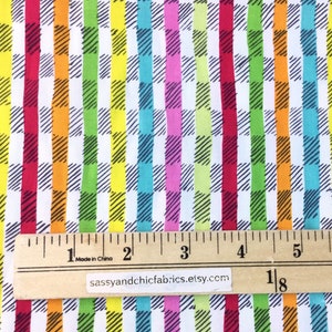 May include: Colorful fabric with a repeating pattern of vertical stripes in red, orange, yellow, green, blue, and pink. Each stripe is overlaid with a black and white checkered design. A wooden ruler shows measurements in inches.
