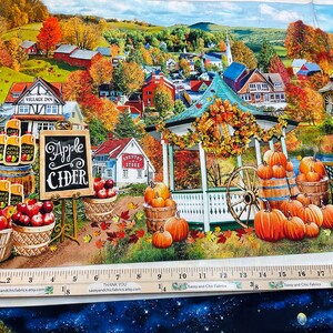 Op de afbeelding: Stoffpaneel met een herfsttafereel met een prieel, pompoenen en een bord voor "Apple Cider". Het kunstwerk toont een schilderachtig dorp met kleurrijk gebladerte, vaten met appels en een watermolen. Een liniaal toont inches.