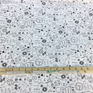 May include: White fabric printed with black math symbols, equations, and the word "MATH." Geometric shapes and numbers are scattered across the fabric. A wooden ruler with inch markings is placed on the fabric.