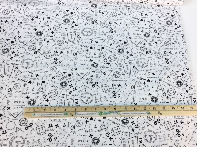 May include: White fabric printed with black math symbols, equations, and the word "MATH." Geometric shapes and numbers are scattered across the fabric. A wooden ruler with inch markings is placed on the fabric.
