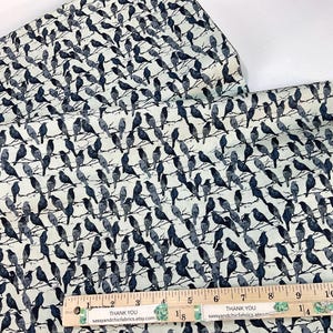 May include: Fabric with a repeating pattern of dark blue birds perched on branches against a light cream background. A wooden ruler with the text "THANK YOU sassyandchicfabrics.etsy.com" is placed on the fabric. The fabric is folded.