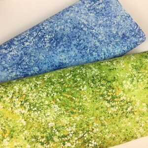 May include: Two rolls of fabric, one in a light blue with white speckles, the other in a vibrant green with white and yellow floral patterns. The fabrics appear to be cotton or a similar material, suitable for quilting or crafting projects.