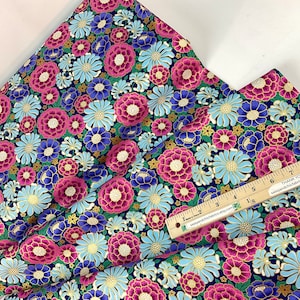 May include: Floral fabric with a dark blue background and a repeating pattern of pink, blue, and gold flowers. A wooden ruler is placed on top of the fabric, showing inch measurements.