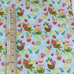 May include: Light blue fabric with a tropical cocktail pattern. The design includes cocktails, pineapples, watermelon, and flowers. A wooden ruler with text is placed on the fabric. The text on the ruler says "Sassy and Chic Fabrics etsy.com".