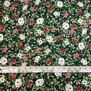K&ouml;nnte beinhalten: Gr&uuml;ner Stoff mit einem Blumenmuster mit roten und wei&szlig;en Rosen, kleinen wei&szlig;en Blumen und roten Beeren. Ein Holzlineal mit Zentimetermessungen liegt auf dem Stoff. Der Stoff hat einen dunkelgr&uuml;nen Hintergrund.