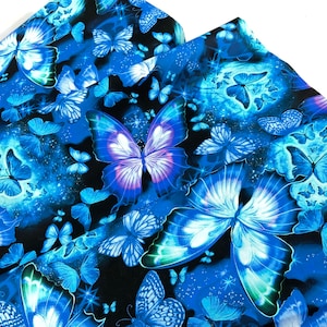 May include: Fabric with a repeating pattern of blue butterflies on a black background. The butterflies vary in size and have detailed wing patterns. Some butterflies are in flight, and others are at rest. The fabric has a celestial theme with stars.