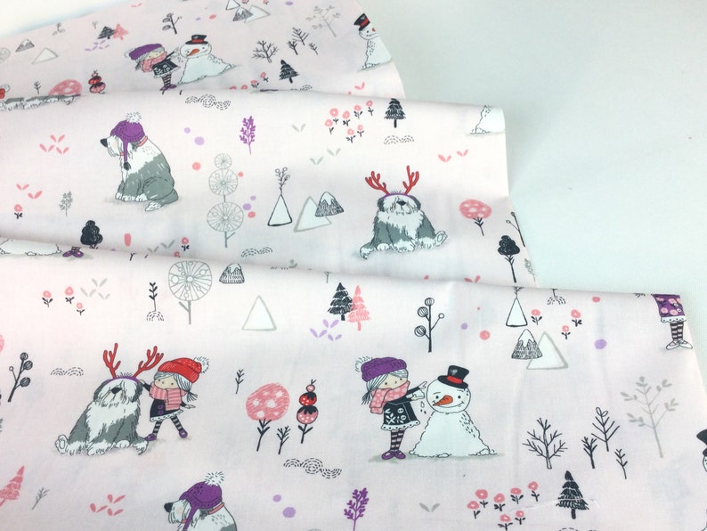 May include: Light pink fabric with a winter-themed pattern. The design features illustrations of children, snowmen, dogs with antlers, trees, and mountains in shades of gray, pink, and purple. The fabric is folded, showing multiple layers.