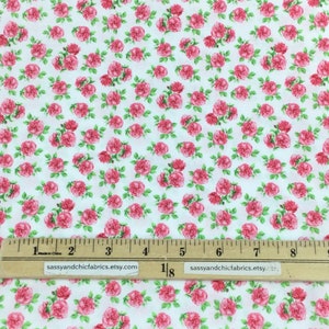 May include: White fabric covered in a repeating pattern of pink roses with green leaves. A ruler with inch markings is along the bottom. The text "sassyandchicfabrics.etsy.com" is printed on the ruler.