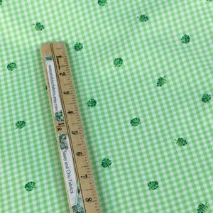 K&ouml;nnte beinhalten: Gr&uuml;ner und wei&szlig;er Vichystoff mit kleinen gr&uuml;nen Blattmustern. Ein Holzlineal mit dem Text "Sassy and Chic Fabrics" liegt diagonal &uuml;ber dem Stoff und misst in Zentimetern.