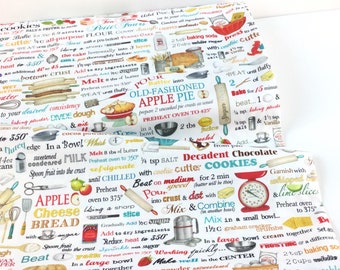Op de afbeelding: Witte stof met een bakthema-ontwerp. De stof bevat verschillende baktermen, illustraties van keukengereedschap en recepten voor appeltaart en koekjes. Het kleurenschema bevat rode, blauwe en groene accenten.