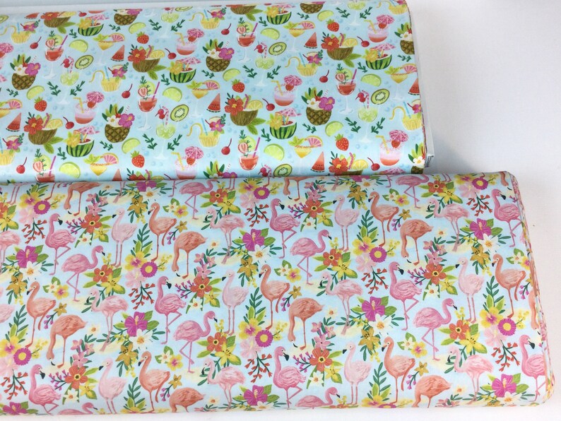 May include: Two rolls of fabric with colorful patterns. One features tropical drinks and fruit on a light blue background. The other has pink flamingos, flowers, and foliage on a light blue background. Both fabrics are likely cotton or a similar material.