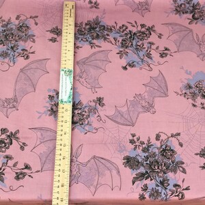 Puede incluir: Tela rosa con un patr&oacute;n repetido de murci&eacute;lagos, flores y telara&ntilde;as. Los murci&eacute;lagos est&aacute;n en vuelo y las flores est&aacute;n agrupadas. Una regla de madera se coloca verticalmente sobre la tela.