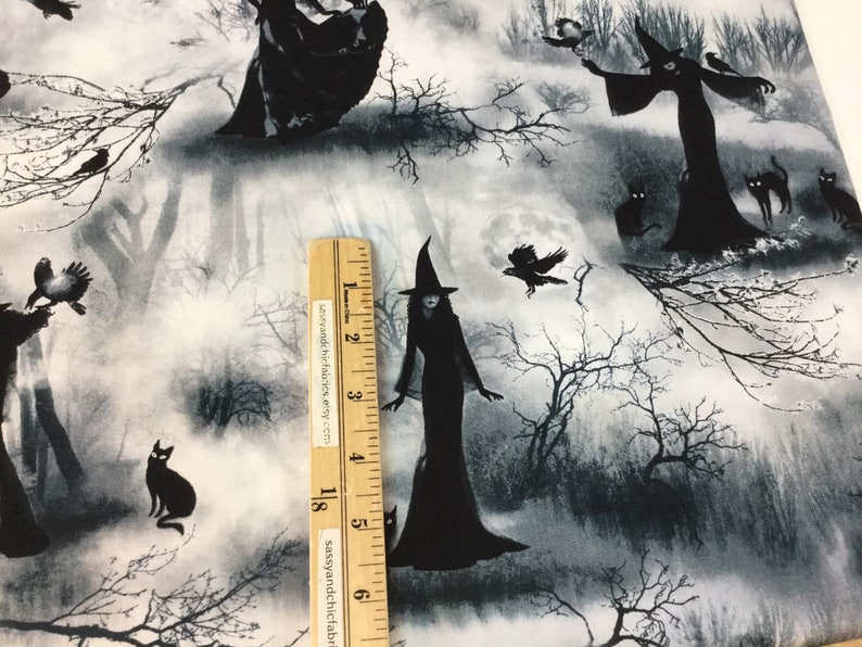 May include: Fabric with a spooky Halloween theme. The design features black silhouettes of witches, cats, and crows against a misty, grayscale forest backdrop. A ruler is placed on the fabric. The text "sassyandchicfabrics.etsy.com" is visible on the ruler.