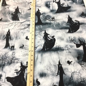 May include: Fabric featuring a repeating pattern of witches in black cloaks and hats, with black cats, crows, and bare tree branches against a misty, moonlit forest backdrop. The ruler shows measurements up to 27 inches.