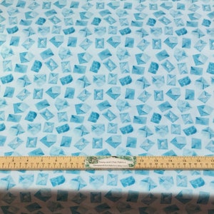 May include: Light blue fabric with a watercolor pattern of scattered envelopes in varying shades of blue. A wooden ruler with inch measurements is placed across the fabric. The fabric is likely for sewing or crafting projects.