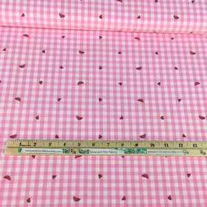 May include: Pink and white gingham fabric with scattered watermelon slice patterns. A ruler with text from sassyandchicfabrics.etsy.com and sassyandchicfabrics.atty.com is placed on the fabric. The fabric is rolled up.
