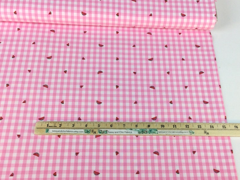 May include: Pink and white gingham fabric with scattered watermelon slice patterns. A ruler with text from sassyandchicfabrics.etsy.com and sassyandchicfabrics.atty.com is placed on the fabric. The fabric is rolled up.