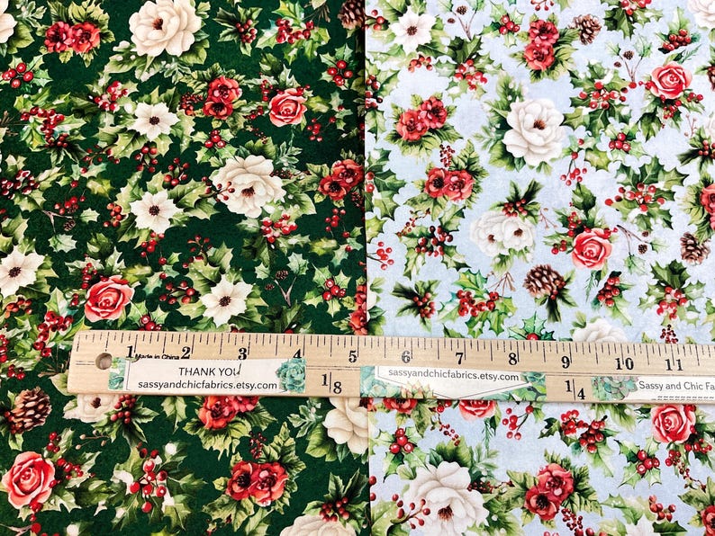 K&ouml;nnte beinhalten: Zwei Stoffmuster mit floralen Mustern. Eines ist dunkelgr&uuml;n mit roten Rosen, wei&szlig;en Blumen und Stechpalmen. Das andere ist hellblau mit dem gleichen floralen Design. Ein Holzlineal zeigt die Ma&szlig;e in Zentimetern an. Der Text "Thank You" und "sassyandchicfabrics.etsy.com" sind sichtbar.