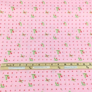 Puede incluir: Tela rosa con un patr&oacute;n repetido de cerezas rojas y hojas verdes, intercaladas con lunares rojos. Una regla con medidas en pulgadas est&aacute; colocada sobre la tela. El texto "sassyandchicfabrics.etsy.com" es visible en la regla.