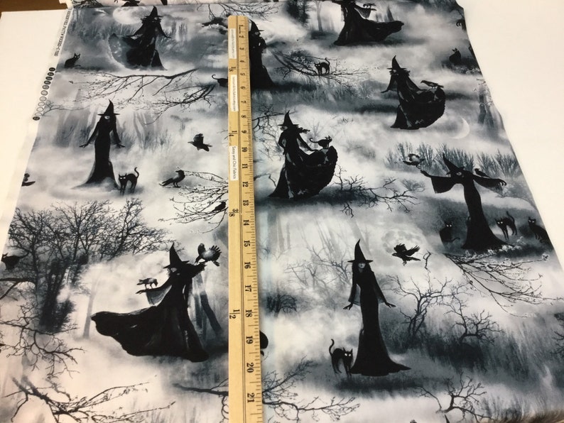 May include: Black and white fabric featuring a repeating pattern of witches in long dresses and pointed hats, with black cats, crows, and bare trees. The fabric has a grayscale color scheme, creating a spooky, Halloween theme.