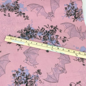 Puede incluir: Tela rosa con un patr&oacute;n repetido de murci&eacute;lagos, telara&ntilde;as y ramos florales en negro y azul claro. Una regla de madera se coloca en diagonal sobre la tela, midiendo hasta 43 cm.