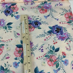 May include: Cream-coloured floral fabric with a pattern of pink, purple, and blue flowers and green leaves. A ruler is placed on the fabric, showing measurements in inches.