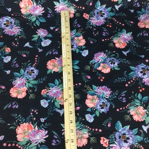 May include: Dark navy fabric with a floral pattern featuring pink, purple, and blue flowers with green leaves. A wooden ruler is placed on the fabric, showing measurements.
