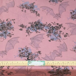 Puede incluir: Tela rosa claro con un patr&oacute;n repetido de murci&eacute;lagos, flores y telara&ntilde;as. Los murci&eacute;lagos est&aacute;n en vuelo y las flores en tonos de negro, gris y azul. Una regla en la parte inferior con medidas en cent&iacute;metros.