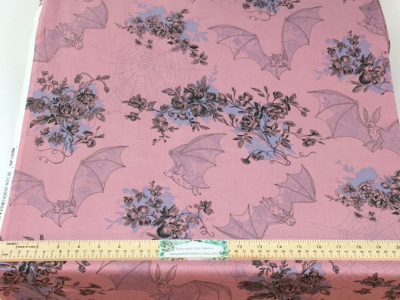 Puede incluir: Tela rosa claro con un patr&oacute;n repetido de murci&eacute;lagos, flores y telara&ntilde;as. Los murci&eacute;lagos est&aacute;n en vuelo y las flores en tonos de negro, gris y azul. Una regla en la parte inferior con medidas en cent&iacute;metros.