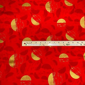 May include: Red fabric with a repeating pattern of gold half-circles and brushstroke textures. The design includes smaller, darker red leaf shapes. A wooden ruler is placed across the fabric, measuring up to 16 inches.