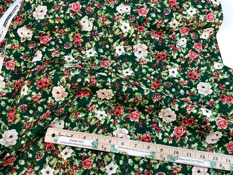 K&ouml;nnte beinhalten: Gr&uuml;ner Stoff mit floralem Muster aus roten Rosen, wei&szlig;en Bl&uuml;ten und Beeren. Auf dem Stoff befindet sich ein Lineal mit dem Text "THANK YOU" und "Sassy and Chic Fabrics". Ideal f&uuml;r N&auml;h- und Bastelprojekte.