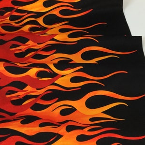 May include: Fabric with a flame design in shades of red, orange, and yellow against a black background. The flames are stylized and appear to be rising. The fabric is folded, showing multiple layers.