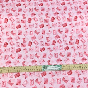 May include: Pink fabric with a repeating pattern of red watercolor envelopes. Each envelope has a small button detail. A ruler with inch measurements is placed on the fabric.