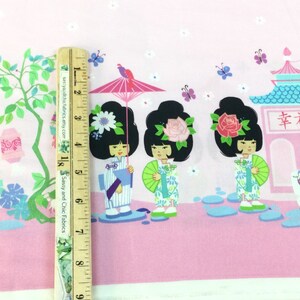 May include: Pink fabric with a Japanese-themed design. Features illustrations of geishas, pagodas, and lucky cats. The fabric includes a ruler for scale, showing the pattern's size.