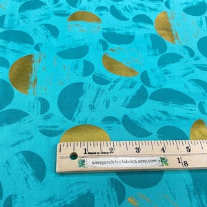 May include: Teal fabric with a pattern of gold and teal half-circles and brushstrokes. A wooden ruler with inch measurements is placed on the fabric. The text "Made in China" and "sassyandchicfabrics.etsy.com" are visible.